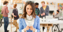 Woman smiling looking down at her phone, people are chatting in the background