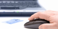 Person using a mouse with a credit card sitting in front and a laptop in the background