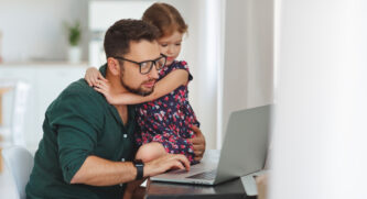 Dad looking at his computer while putting his arm around his daughter while she watches