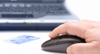 Person using a mouse with a credit card sitting in front and a laptop in the background